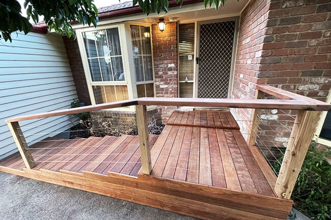 Wooden ramp with railing leading to a house's front door, featuring brick walls and large windows.