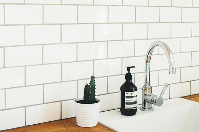 Modern kitchen sink with chrome faucet, dark Aesop soap bottle, and a small cactus in a white pot.