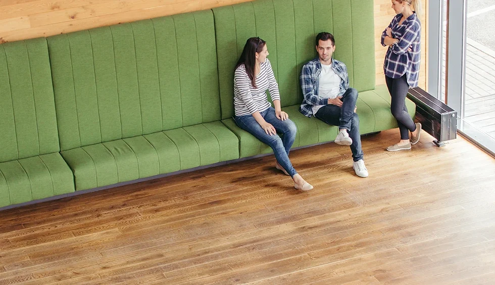 Cozy café with green seating, two people chatting and a third standing nearby in conversation.